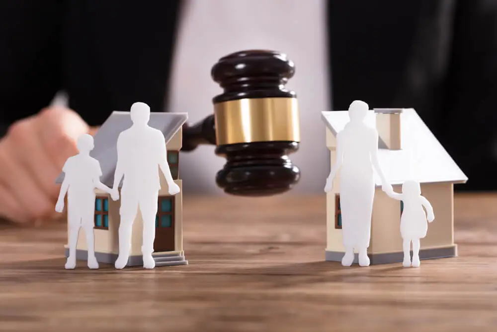 Judge Striking Gavel Between Family Paper Figure Cut Out And Split House On Top of Desk